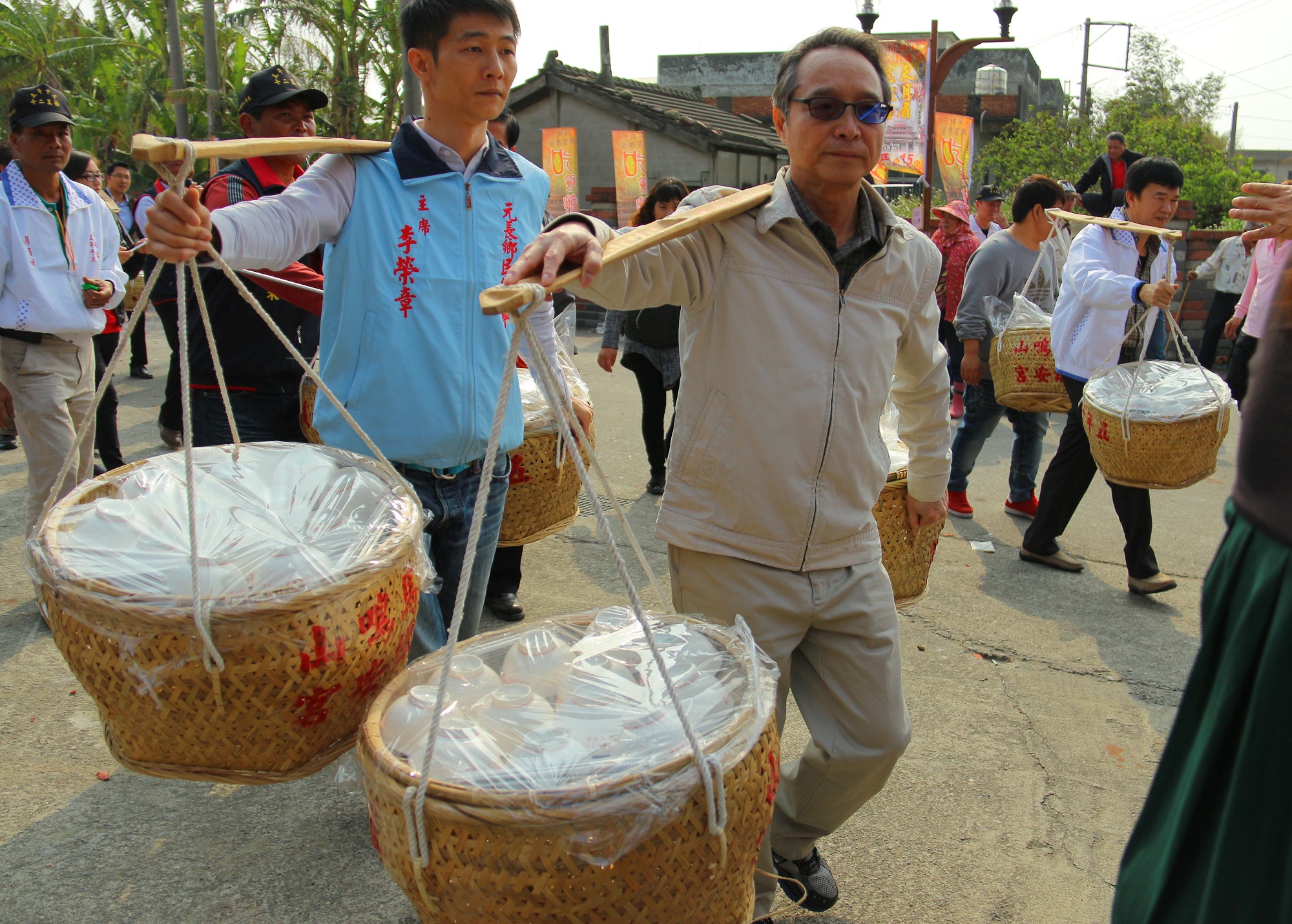 中心代理執行長詹澈與村民們肩挑飯擔，裝著油飯、羊肉湯、貢丸湯等美食走進田野